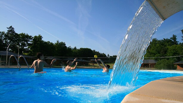 A swimming pool with a water slide, clear blue water, and a fence in the background.