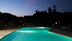 Una piscina al crepuscolo, circondata da alberi e luci lontane.