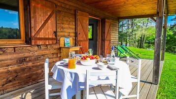 A wooden cabin with a dining table set for breakfast, a green lawn, and a clear view of the surrounding forest.