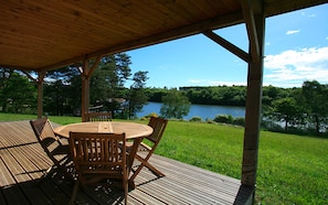 Une terrasse en bois avec une table ronde et des chaises, donnant sur un lac et une végétation luxuriante.