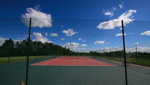 A tennis court enclosed by a chain-link fence with a clear sky and trees in the background.