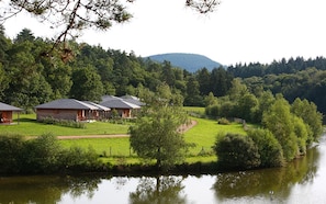A lakeside property with wooden cabins, a grassy area, and a forested hill in the background.