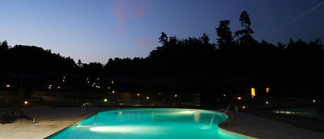 Una piscina al anochecer con árboles circundantes y luces a lo lejos.