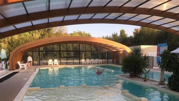 Une piscine intérieure dotée d’une structure en arc de bois au-dessus, entourée de chaises longues et d’un petit espace piscine.