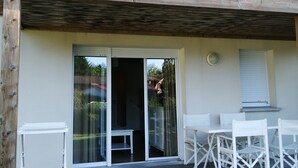 Une terrasse en bois dotée d’un espace couvert, une porte-fenêtre coulissante donnant sur un patio, ainsi qu’une petite table et des chaises.