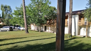 Une zone herbeuse avec une table en métal blanc, des arbres et un bâtiment doté d’un toit en tuiles.
