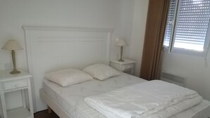 Une chambre à coucher avec un lit, deux tables de chevet et une fenêtre avec des stores.