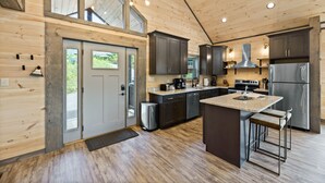 A modern kitchen with wooden walls, a large island, stainless steel appliances, and a high ceiling with exposed beams. - BRADN NEW Luxury Cabin! The ELM/PanoramicMountainView/Modern/LARGE DECKs (Gatlinburg)