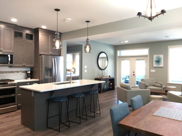 A modern kitchen with a central island, bar stools, and a dining area with a wooden table and chairs.