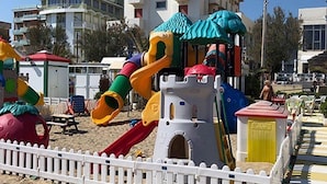 A beach playground with slides and climbing structures, surrounded by a white fence. - Hotel International (Senigallia)