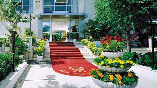 A hotel entrance with a red carpet leading to a staircase, surrounded by potted plants and a large flower arrangement. - Hotel International (Senigallia)