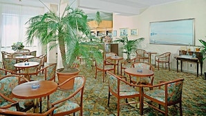 A hotel lobby with round tables and chairs, potted plants, and a large window with a view. - Hotel International (Senigallia)