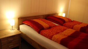 Una cama doble con ropa de cama rojo anaranjada, un cabecero de madera y lámparas de noche.