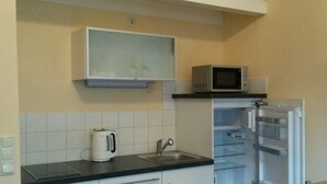 Cocina compacta con armarios blancos, microondas, pileta y tetera.