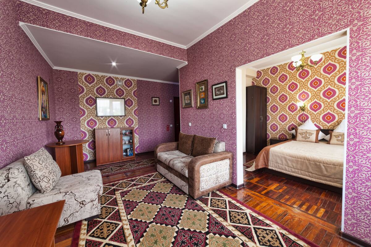 Ein Zimmer mit gemustertem Wandpapier, einer Couch, einem Bett und einem Holzboden.