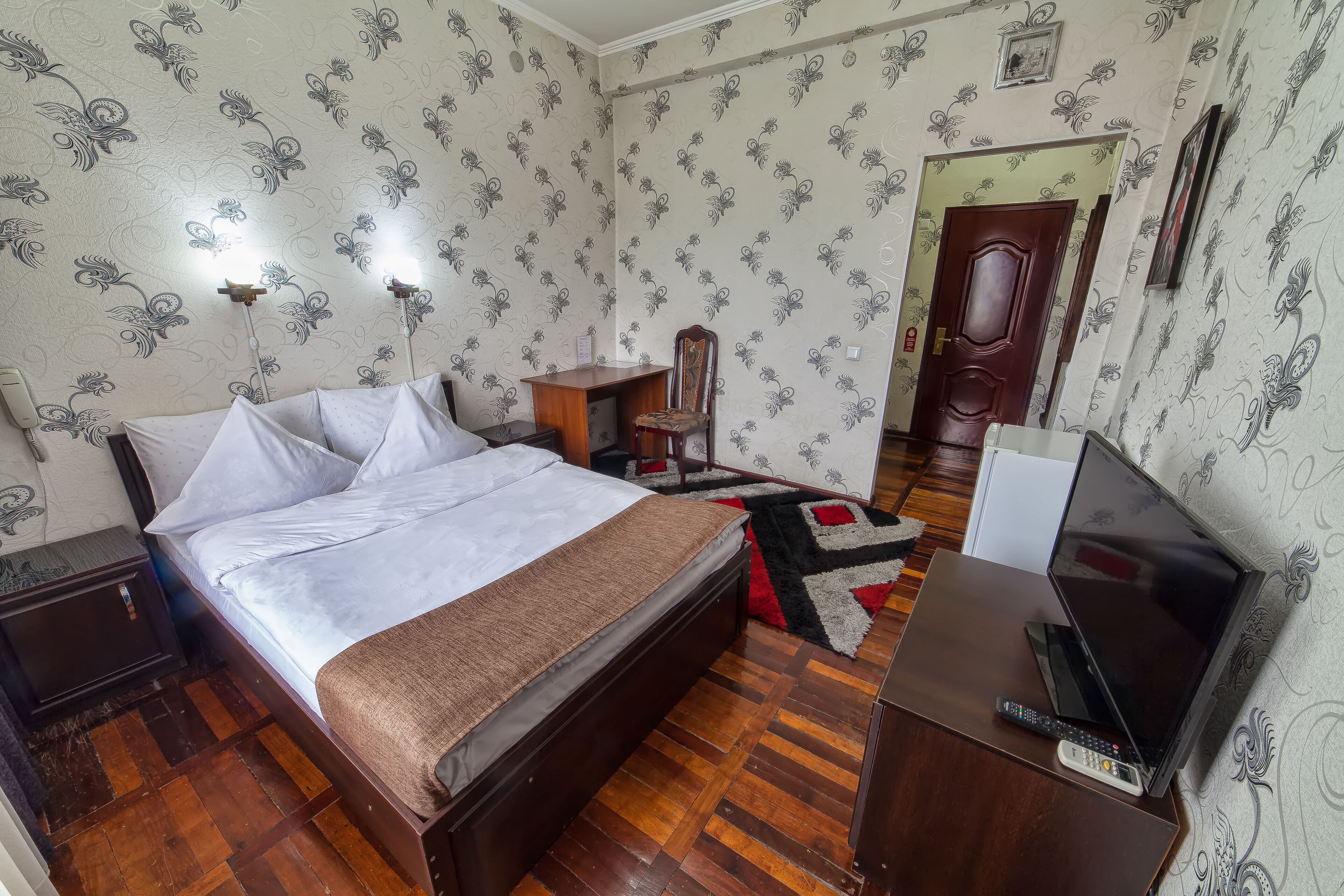 Una camera da letto con un letto di legno, una scrivania con televisore, una sedia e una lampada.