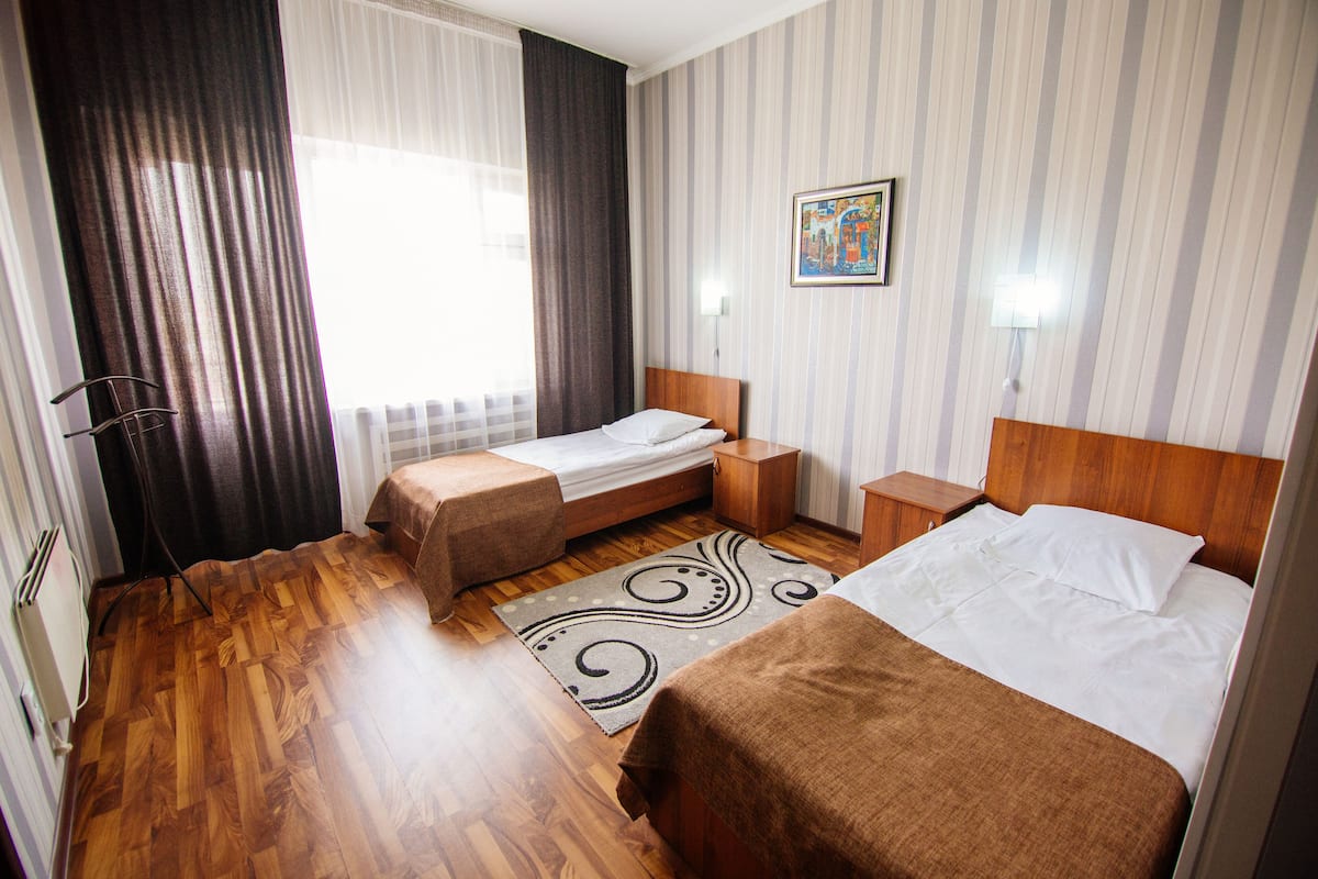Ein Hotelzimmer mit zwei Einzelbetten, Holzboden, einer gestreiften Wand und einem Fenster mit Vorhängen.