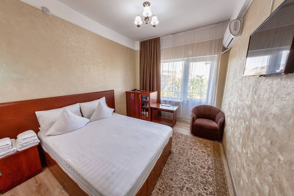Ein Hotelzimmer mit Bett, Schreibtisch, Stuhl, Fernseher und einem Fenster mit Vorhängen.