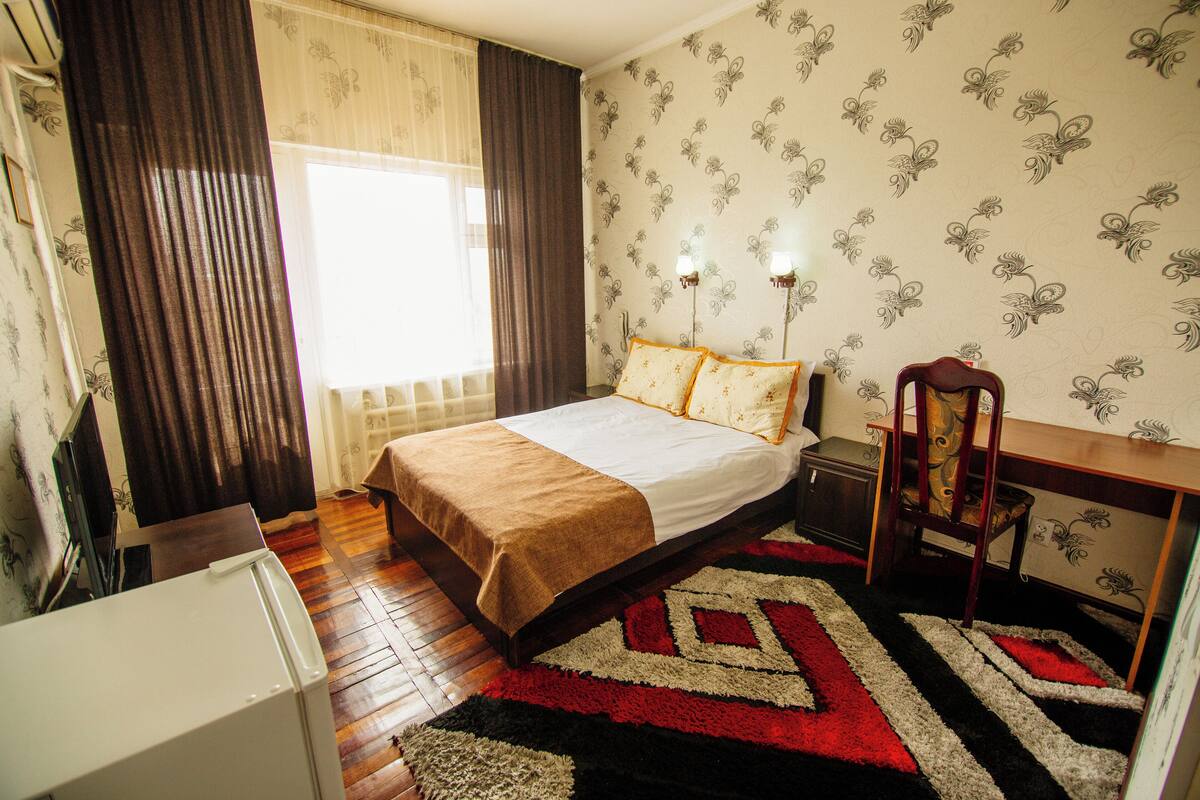 Ein Schlafzimmer mit Bett, Schreibtisch, Stuhl, Nachttisch und einem Fenster mit Vorhängen.