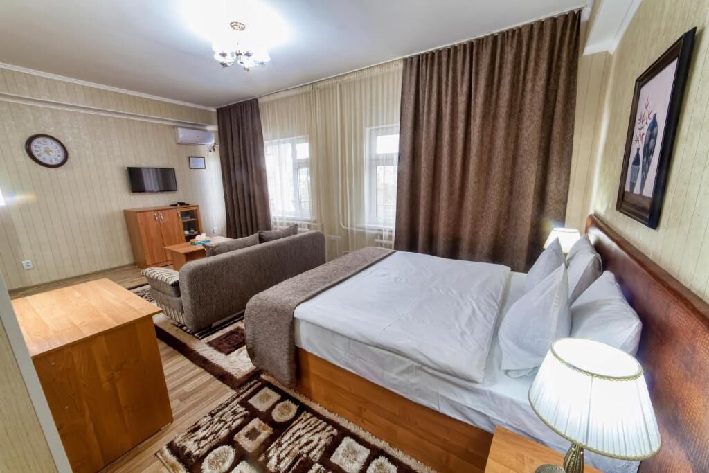 Habitación de hotel con cama, sofá, televisión, armario de madera y ventana con cortinas.
