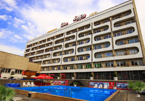 Un hotel con diversi balconi, piscina e area salotto all'aperto con ombrelloni.