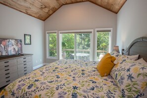A bedroom with a large bed, a dresser, a TV, and a balcony with a table and chairs.