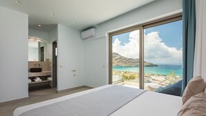 Ein Schlafzimmer mit einem großen Bett, ein Badezimmer mit Waschbecken und Regalen sowie ein Balkon mit Meerblick.