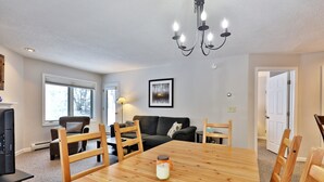 Un comedor con mesa de madera, sillas, lámpara de araña, sofá y televisor.