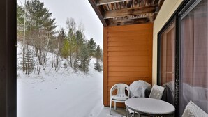 Un patio cubierto de nieve con una mesa y sillas, un muro de madera y una vista de árboles nevados.
