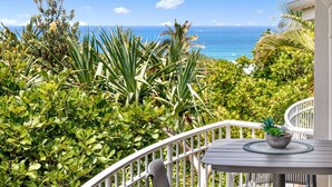Un balcone con vista sull'oceano, immerso nel verde e con ringhiera bianca.
