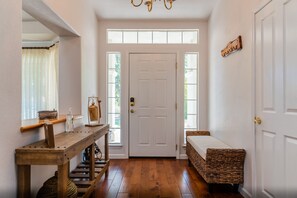 A hallway with a wooden bench, a small table with a book and a bottle, and a wicker bench by the door.