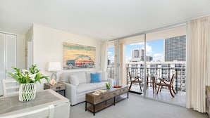 A modern living room with a sofa, coffee table, and a balcony with a city view. - HIGH Floor w/Canal, Mtn and Partial Ocean Views! AC, W/D, WiFi, Pool,Parking! (Honolulu)