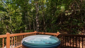 Un jacuzzi en una terraza de madera rodeado por una barandilla de madera, ubicado en un área boscosa.