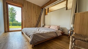 A bedroom with a wooden floor, a bed with a headboard, a ladder, and a window with a view of greenery. - Domaine Taureau, Morvan Regional Nature Park (Saint-Brisson)