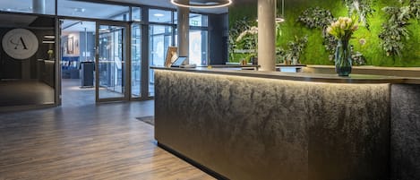 A reception area with a modern design, featuring a reception desk, a clock, and a green wall with plants.