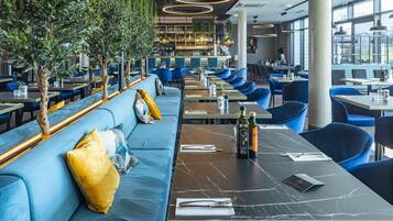 Un interno ristorante moderno con sedute blu, un'area bar e piante pensili.