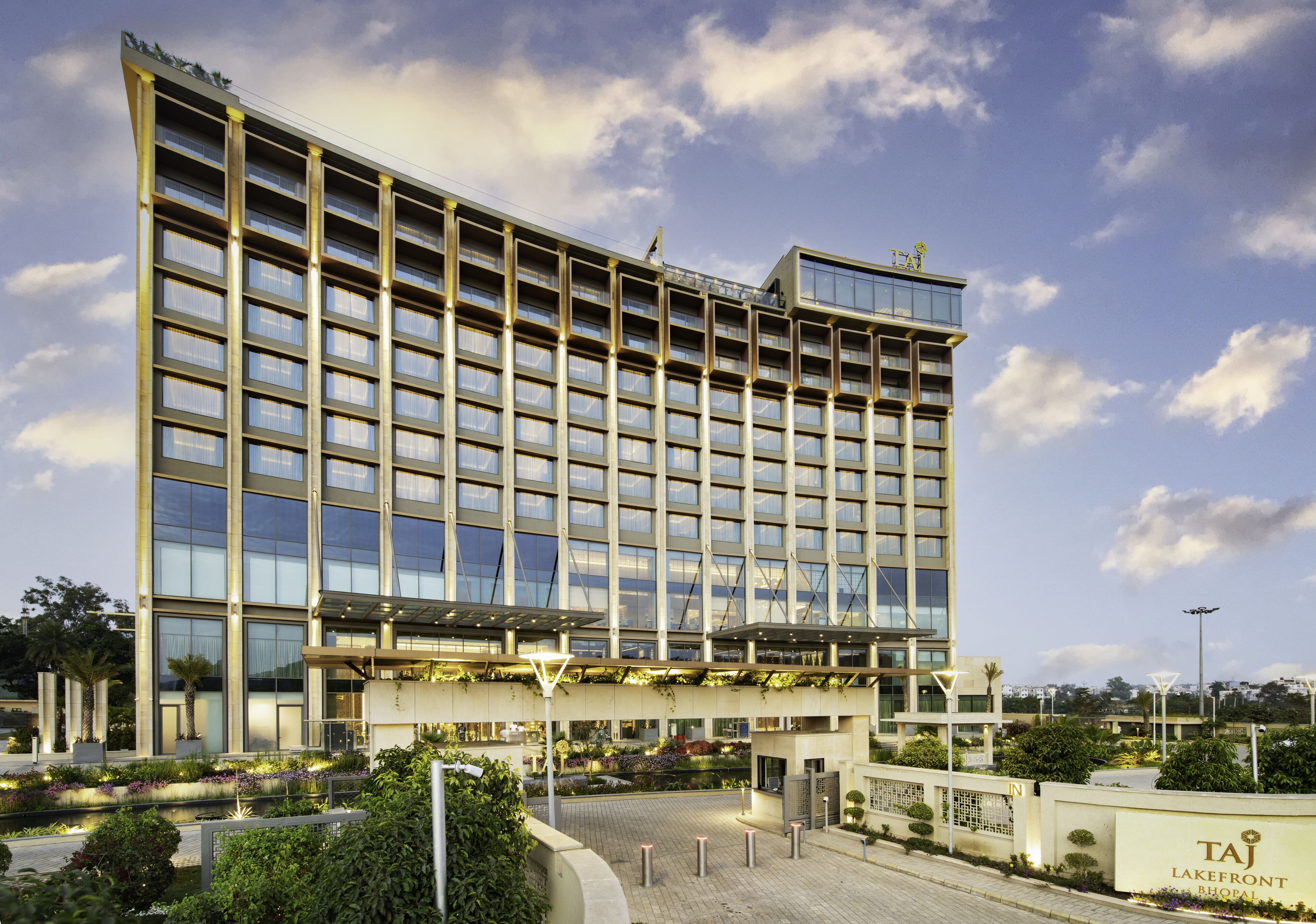 A modern hotel building with a large glass facade, multiple floors, and a landscaped entrance area.