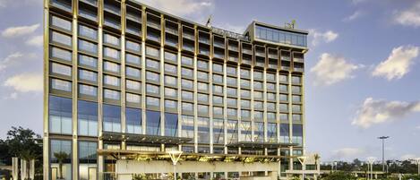 A modern hotel building with a large glass facade, multiple floors, and a landscaped entrance area.