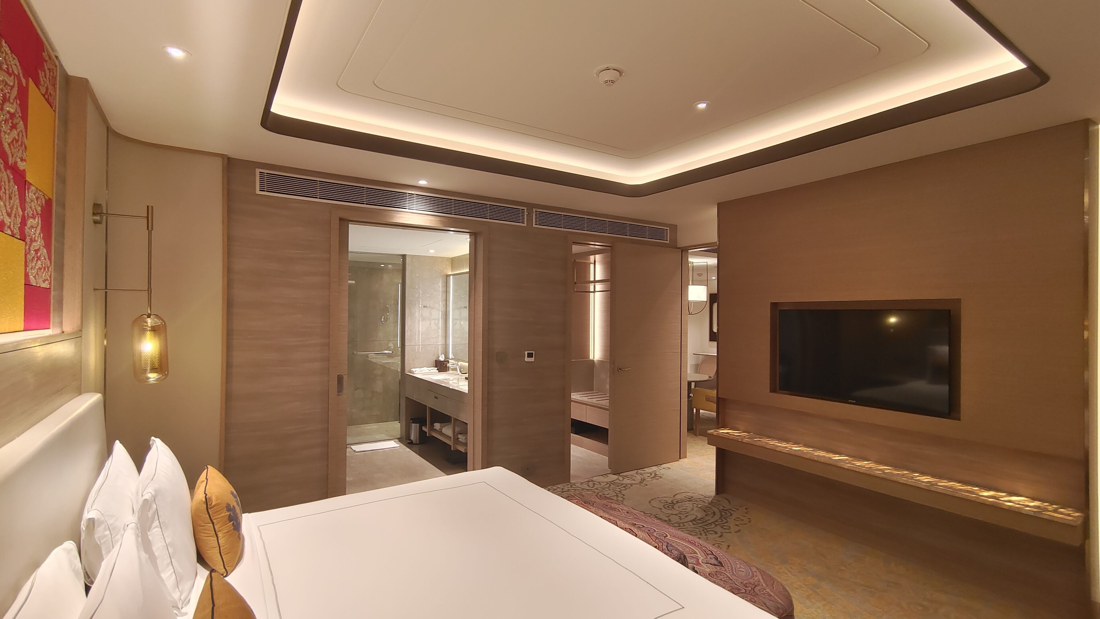 A modern hotel room with a large bed, a TV mounted on the wall, and a walk-in closet.