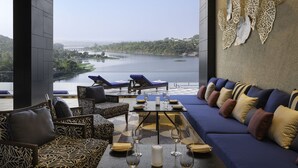 A modern lounge area with a view of a lake and bridge, furnished with sofas, chairs, and a table set for dining. - Taj Lakefront Bhopal (Bhopal)