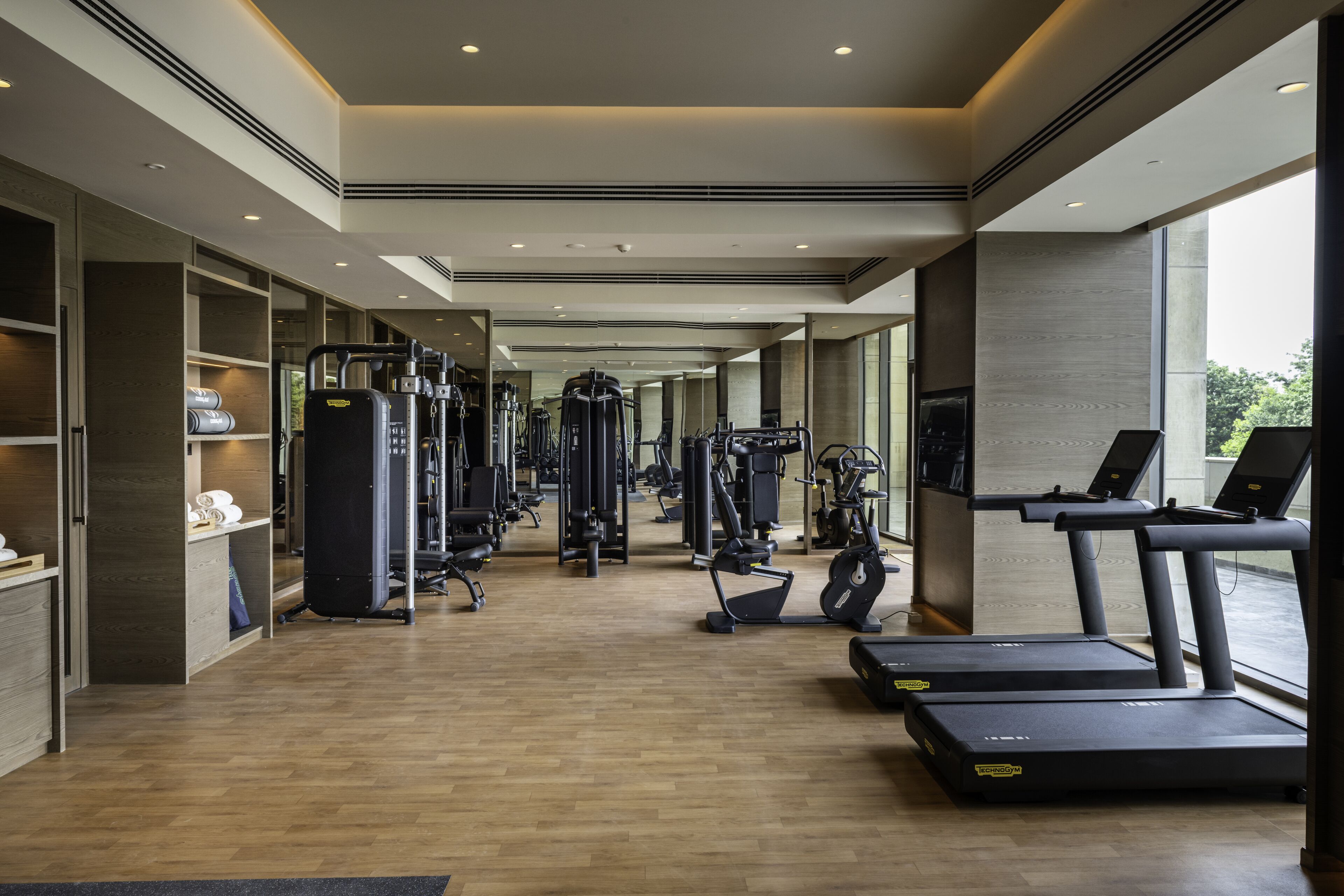 Une salle de sport moderne équipée de divers appareils d’exercice, notamment des tapis de course et des appareils de musculation, et dotée de grandes fenêtres qui laissent entrer la lumière naturelle.