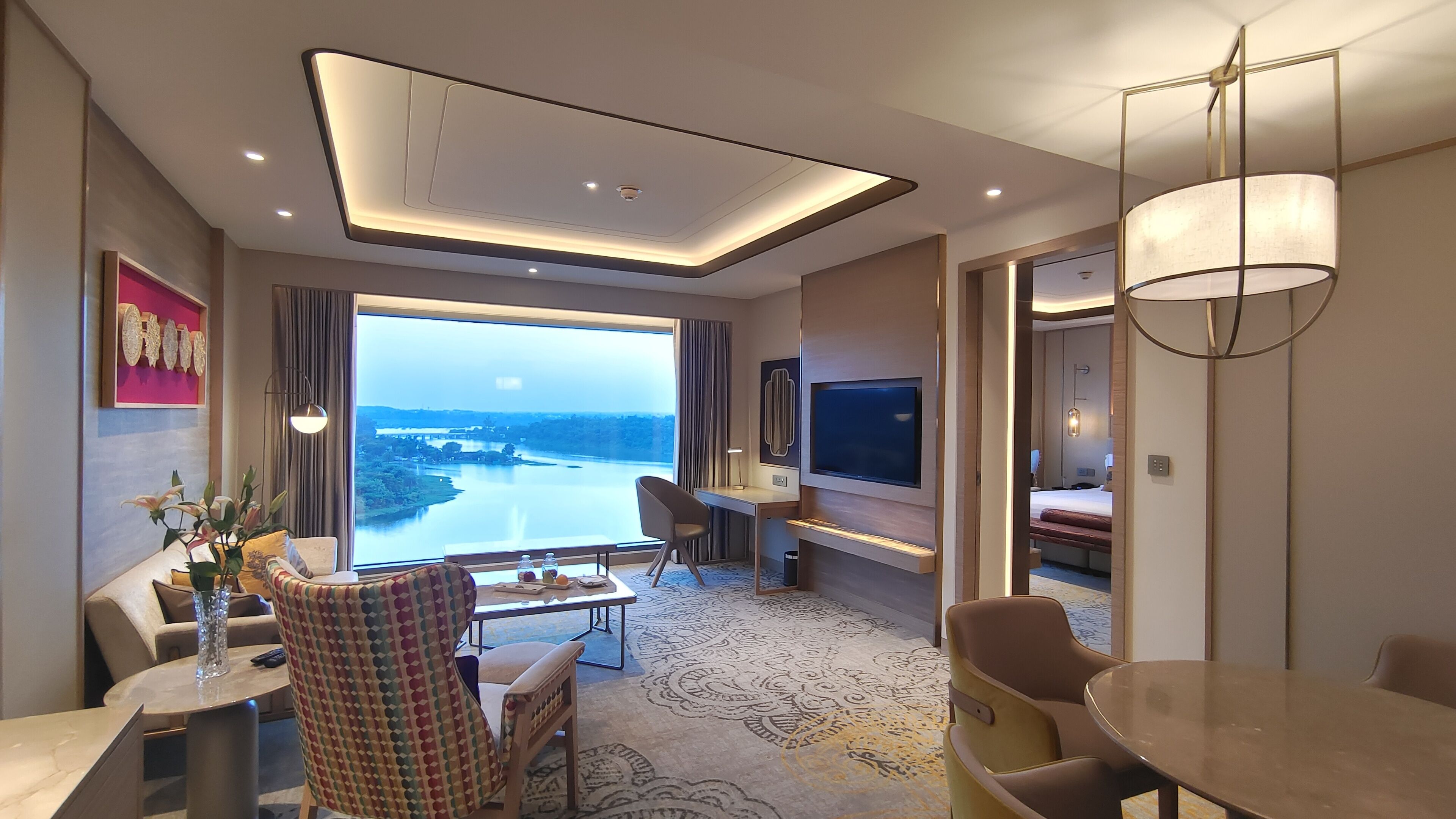 A modern hotel room with a large window offering a scenic view of a river and hills.