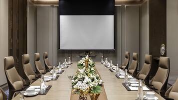 Une salle de conférence avec une longue table, des chaises de couleur beige et un grand écran à l’avant.