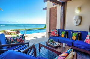 A beachside lounge with a view of the ocean, a pool, and a seating area with colorful cushions.