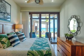 A bedroom with a bed, a wooden dresser, a mirror, and a view of the ocean.