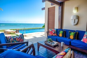 A beachside lounge with a view of the ocean, a pool, and a seating area with colorful cushions.