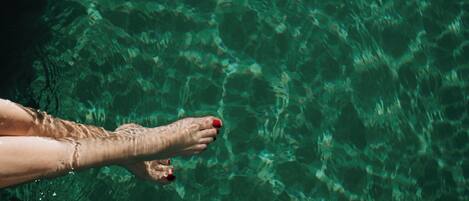A clear view of a swimming pool with visible water ripples and a person's arm and hand reaching towards the water.