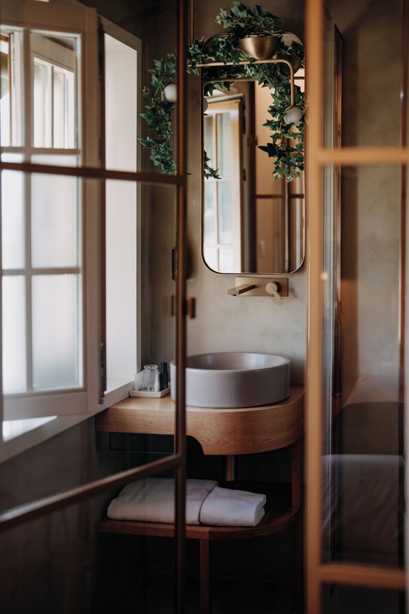 Un baño con un lavamanos redondo, un espejo y una ventana.