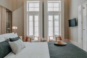 Una habitación de hotel con una cama grande, dos sillas, un televisor y vistas a través de puertas dobles.