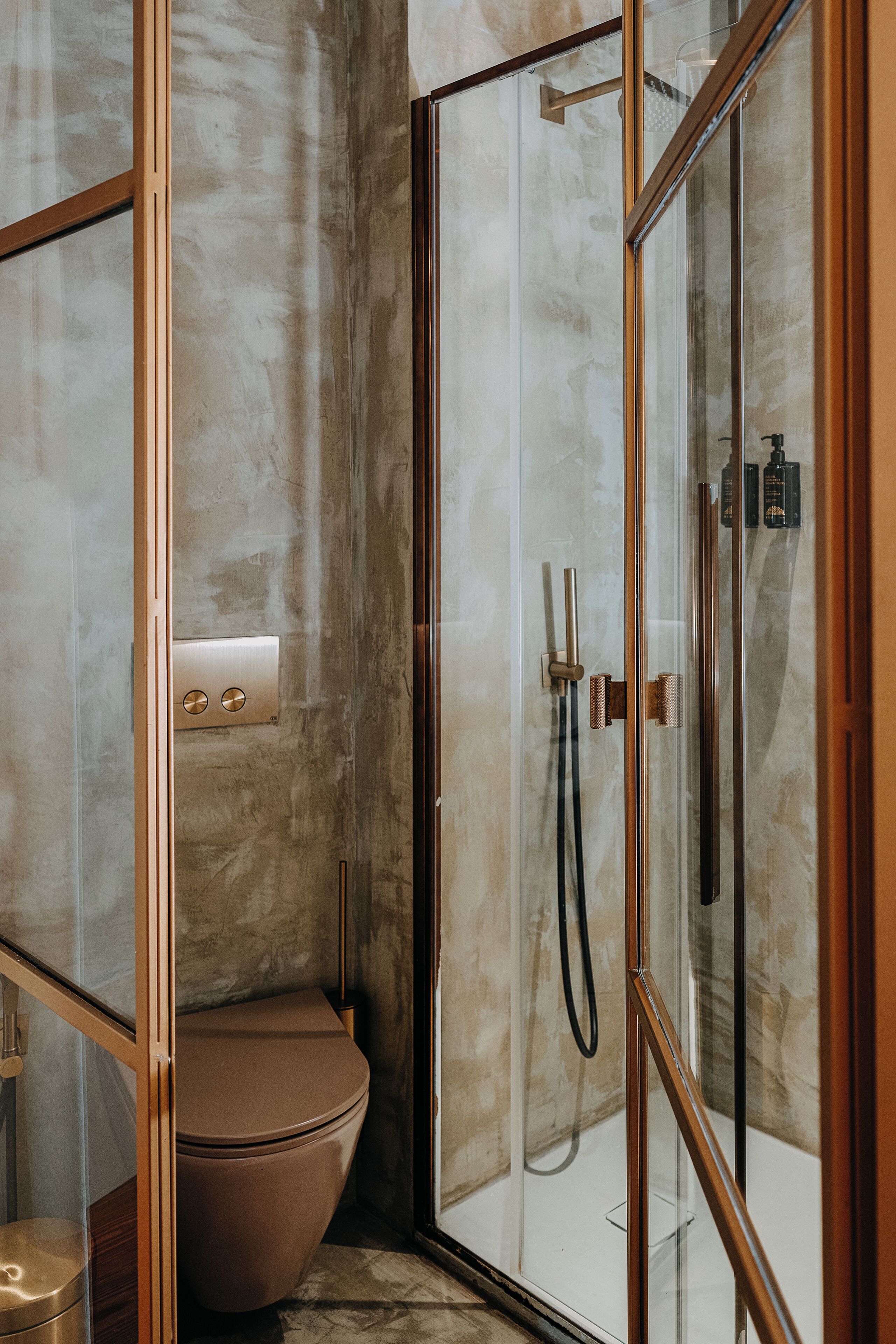 Un baño moderno con ducha envuelta en vidrio, pared de mármol y inodoro de madera.
